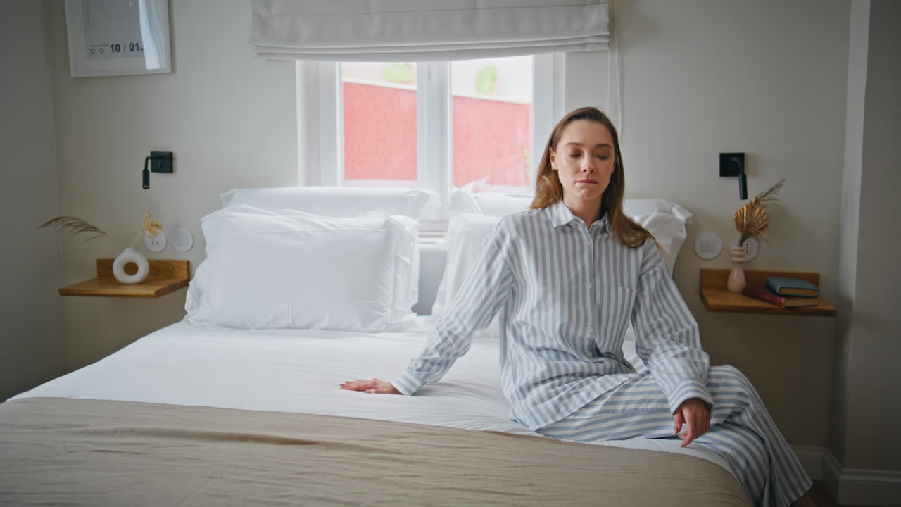 Woman enjoy comfortable bed sitting modern home bedroom in striped pajamas