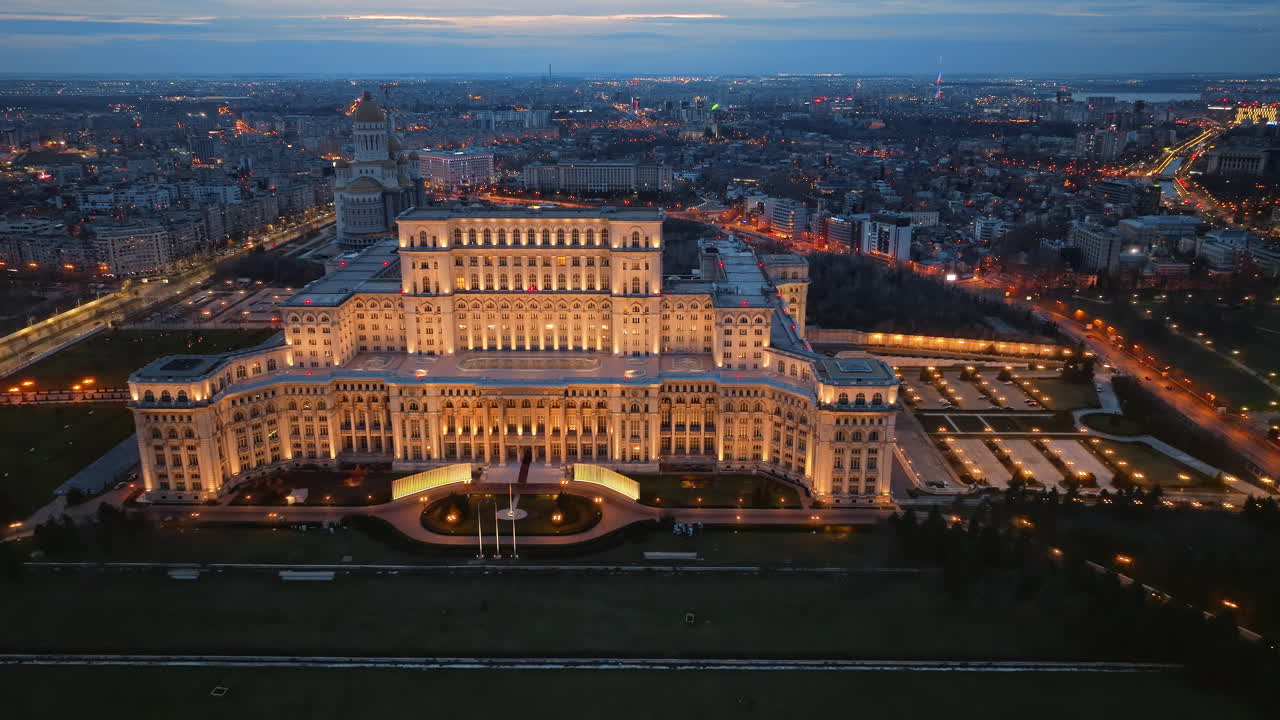 Aerial drone view of illuminated Palace of the Parliament in Bucharest downtown in the evening. Multiple districts around. Romania