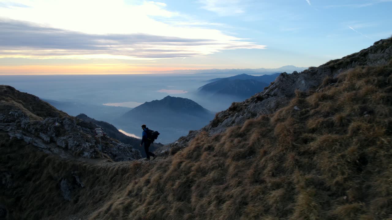 이탈리아의 레세고네 산꼭대기에서 해가 지는 동안 산책하는 산책객, 배경에는 알프스 산맥과 호수의 멋진 전망이 있습니다.