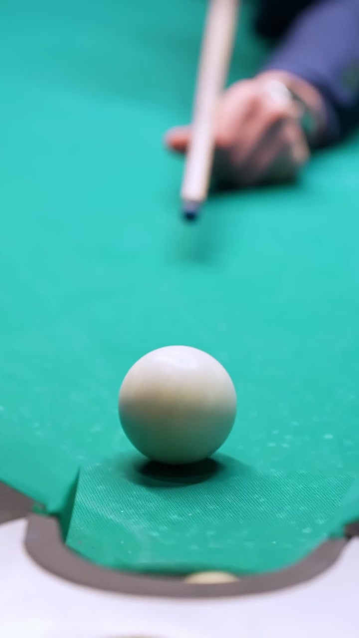 Close-up vertical billiards shot as cue ball and striped ball drop into corner pocket on green felt table, capturing skillful double pot in a bar game.