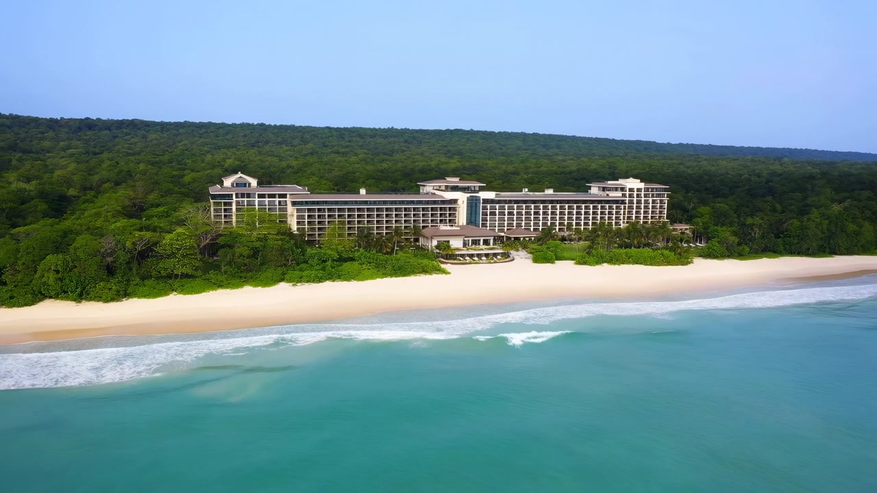 Resort aereo su spiaggia tropicale isolata che mostra un hotel di lusso sullo sfondo di una fitta foresta e un oceano turchese