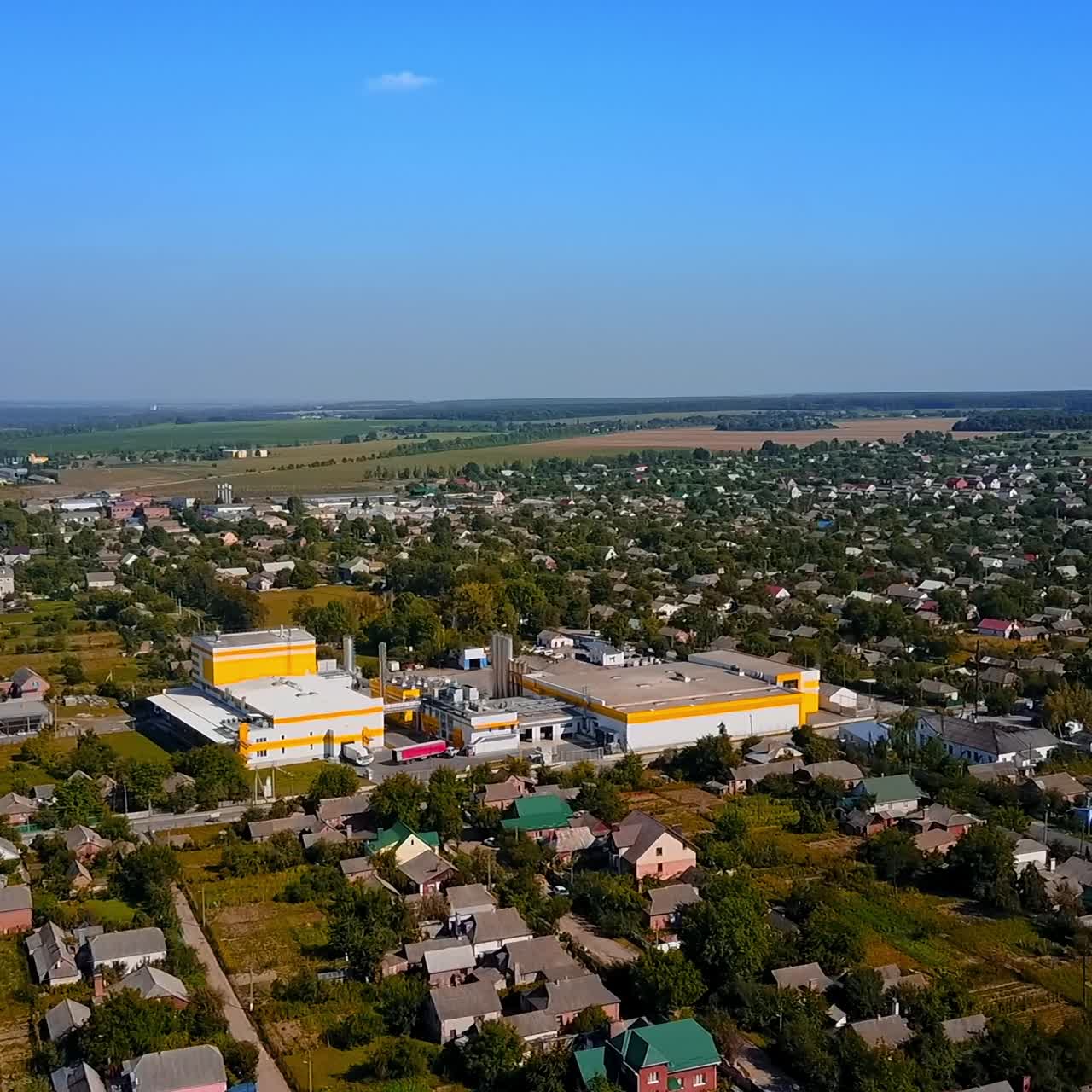 Flying above the provincial town with private cottages. Farmlands and forests at backdrop. Aerial view