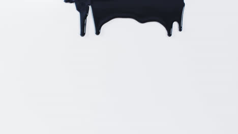 Close-up-of-black-paint-shapes-on-white-background-with-copy-space,-slow-motion