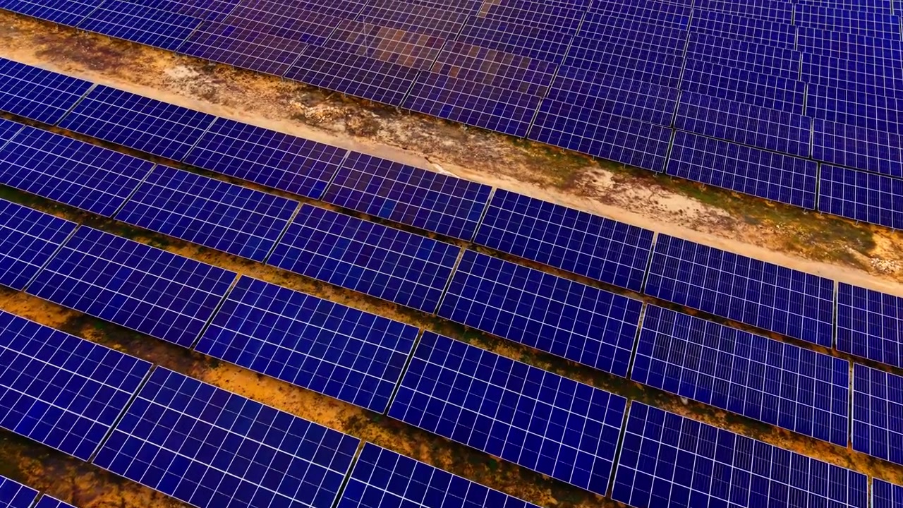 File di pannelli solari che coprono un campo, Bulgaria. Prospettiva aerea angolata di moduli fotovoltaici blu densi in linee parallele con terreno sabbioso tra le file sotto la luce del giorno