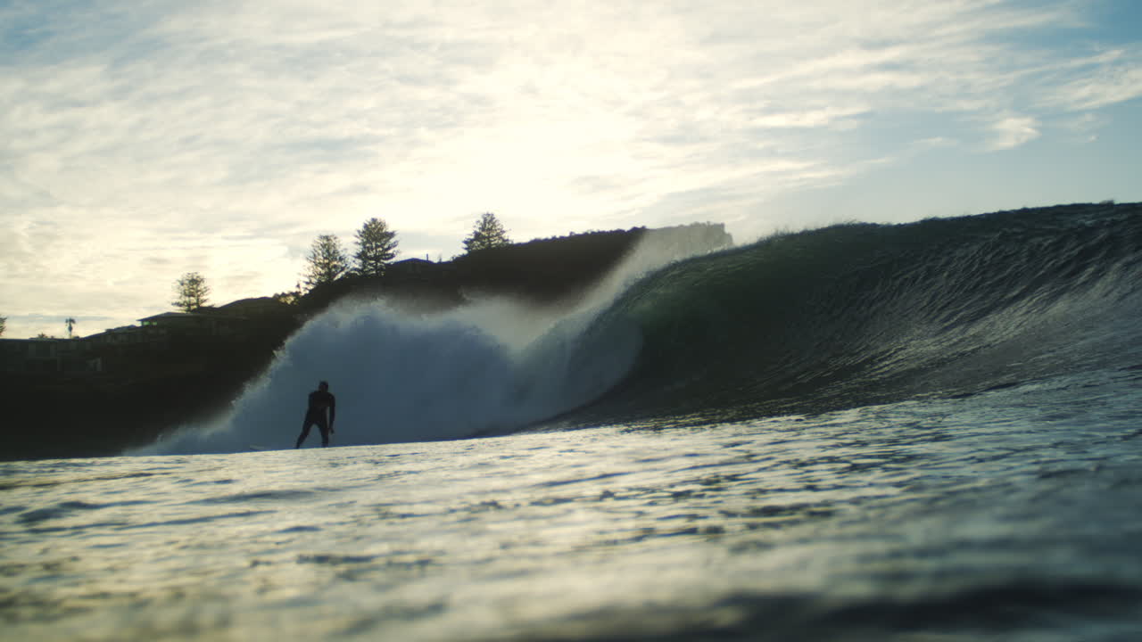 Surfer gets barreled in shorebreak as sunrise light glistens over breaking wave in slow motion