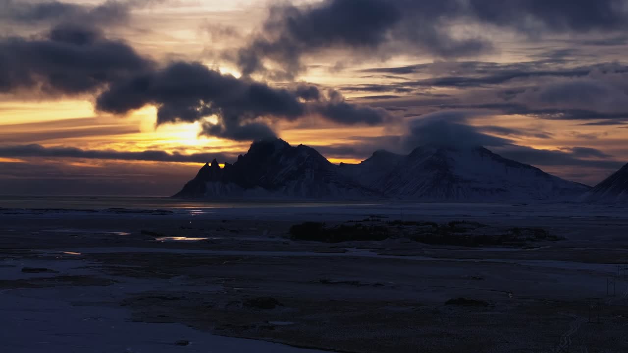 Dramatic glowing sunset beyond Vestrarhorn landmark, Iceland winter landscape - aerial 4k