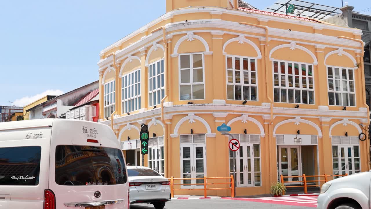 Vehicles and pedestrians navigate a vibrant street in Old Town Phuket, showcasing colorful architecture under bright daylight