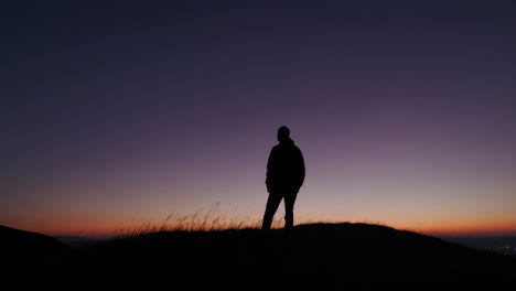 silhouette of a man contemplating a sunset on a hill