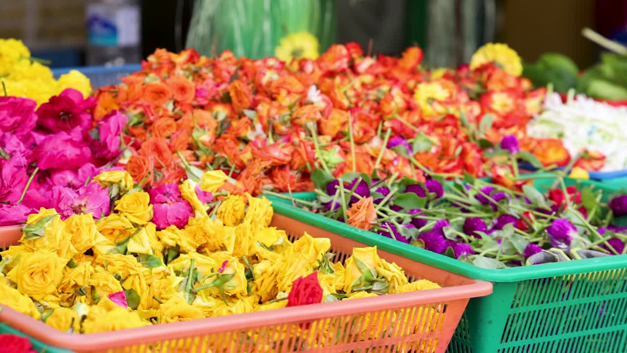 Vibrant marigolds, roses, and other flowers arranged in baskets at an outdoor market in Singapore. Bright daylight, smooth lateral camera pan, lively atmosphere