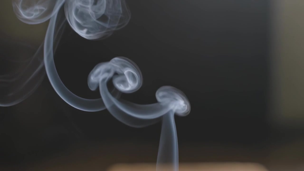 Forming thin smoke column shedding toroidal rings drifting leftward at dim tabletop from ember