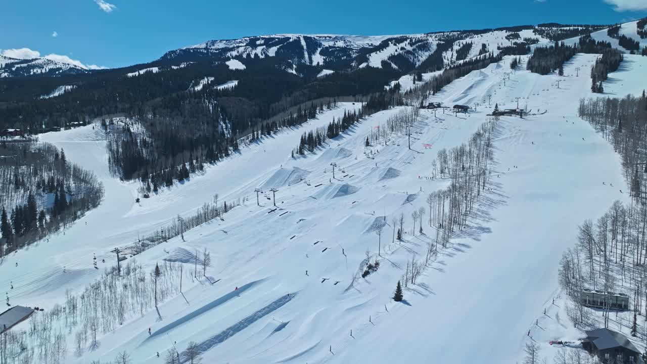 Wide drone view of ski lifts and trails across mountain slopes in bright midday winter light, Snowmass Colorado