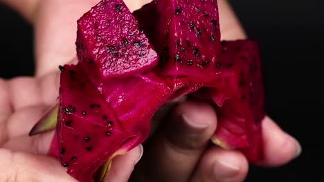 hands holding and displaying vibrant red dragon fruit slices with visible seeds.