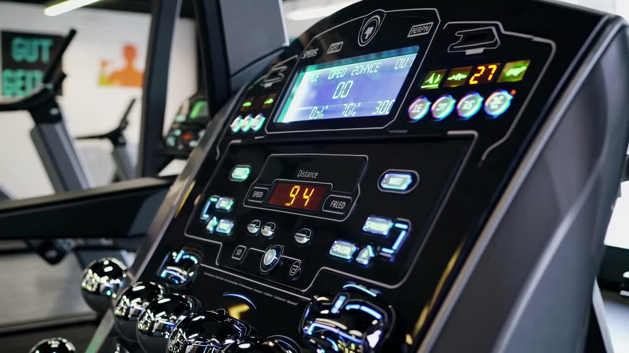 Close-up, angled shot of a treadmill control panel in a gym setting, highlighting the digital