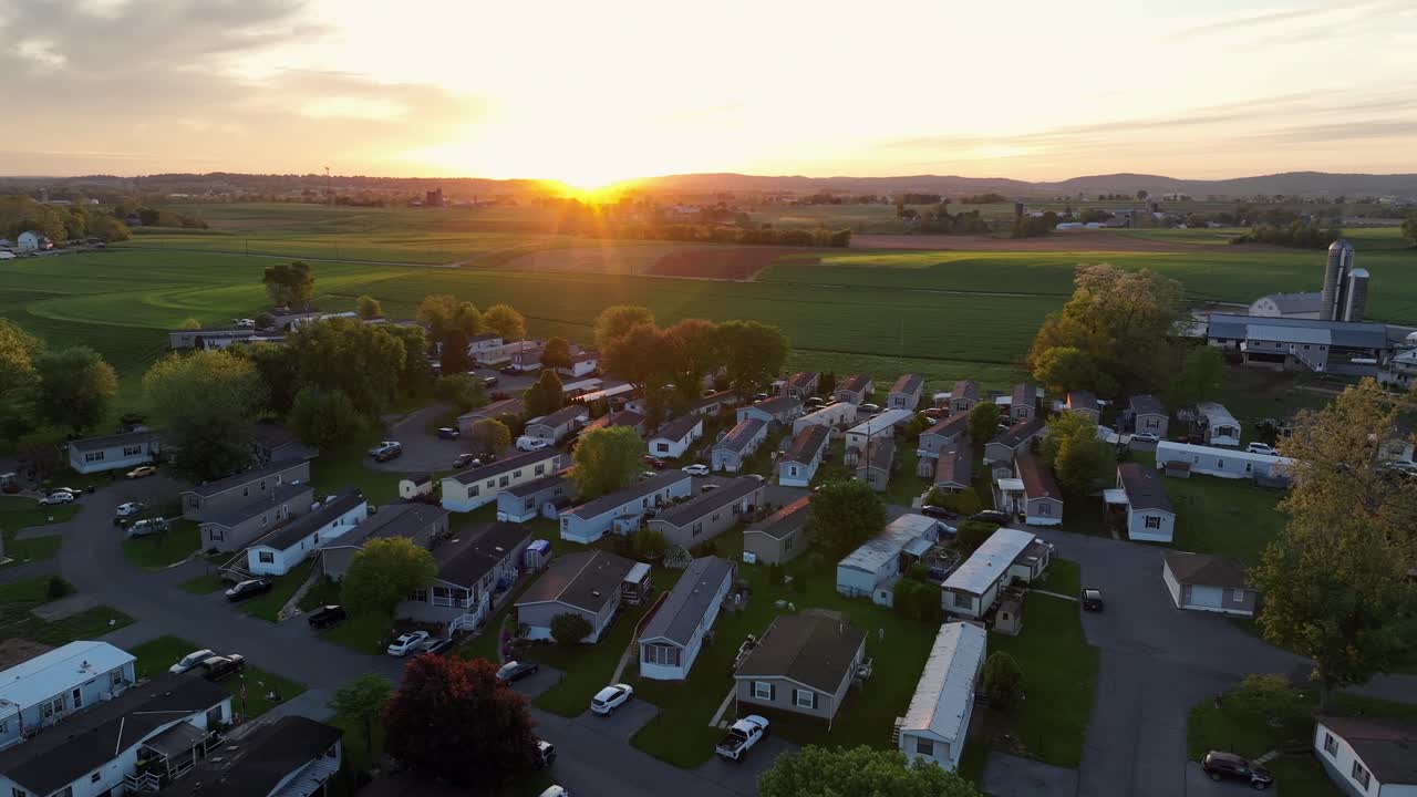 Mobile trailer homes and Silo storage of farm during golden sunset in America. Aerial approaching wide shot. Green farm fields in rural area of Pennsylvania.