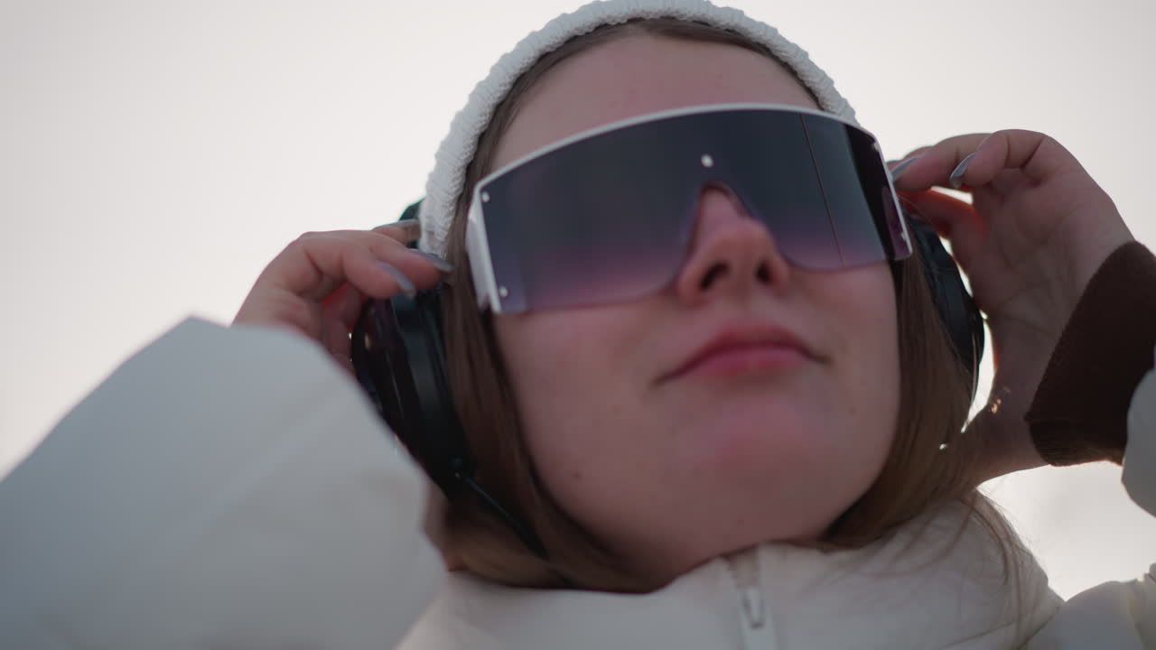 Close up of student wearing over ear headphones smiling as snow glistens under sun while she dons beanie and coat enjoying crisp winter vibe and music driven joy capturing youthful creativity