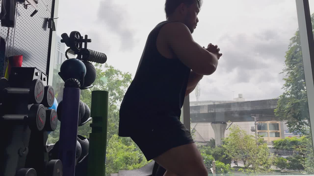 Two athletic men perform synchronized bodyweight squats in a modern gym with city views