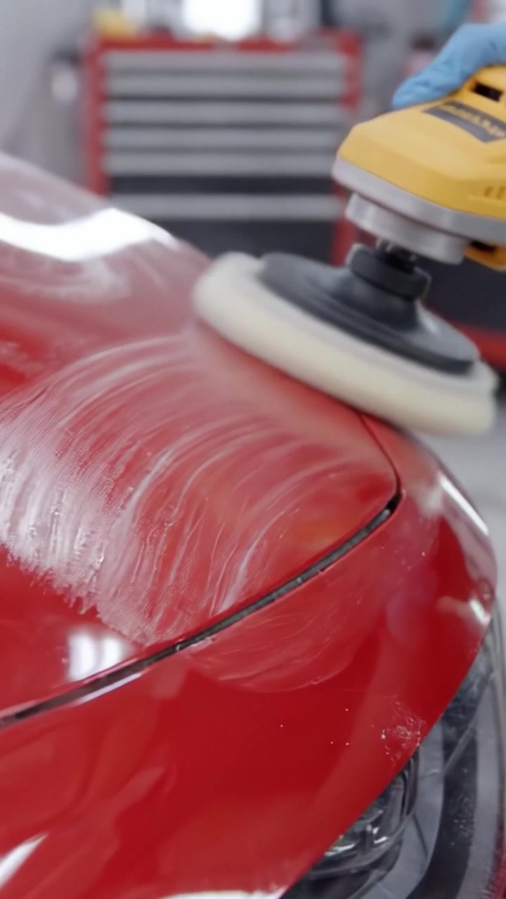 A Professional Detailing Session Focused on Restoring the Shine of a Red Car's Surface with a Polishing Machine in a Workshop Environment