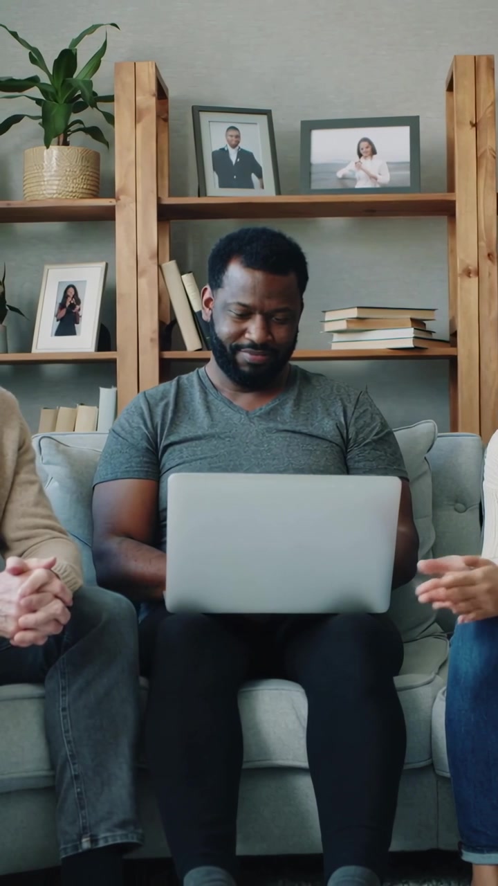 Vertical video: Glancing at laptop, centered man in grey T-shirt typing and reviewing work on sofa