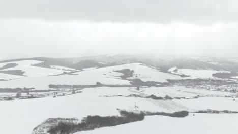 aerial right pan through snowed in hill landscape with town and mountains in background