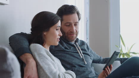 pareja feliz relajándose en casa usando el teléfono inteligente juntos comprando en línea disfrutando de navegar por internet relajándose en el sofá