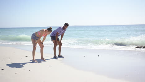 una joven caucásica y un hombre biracial están haciendo ejercicio en una playa soleada con espacio para copiar
