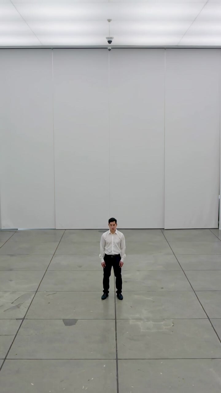 Vertical video: Standing man in white shirt black pants shifting in empty hall while camera records