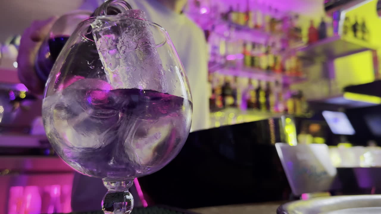 cocktail with ice in large glass at vibrant bar with colorful lights
