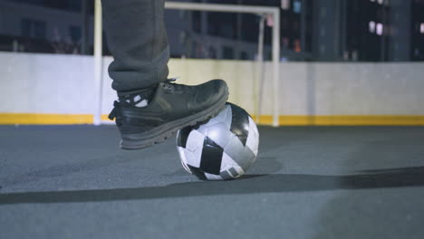 close up back view of soccer player resting one foot on soccer ball on an outdoor sports field, wearing athletic shoes and sweatpants, goalpost visible in background