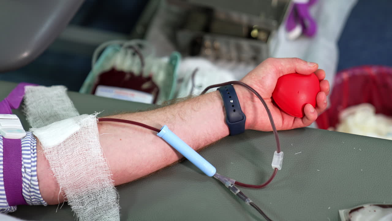Arm of an unrecognized man donating his blood. Machine with a plastic bag filled with blood works at backdrop in blur.