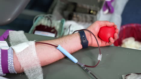 arm of an unrecognized man donating his blood. machine with a plastic bag filled with blood works at backdrop in blur.
