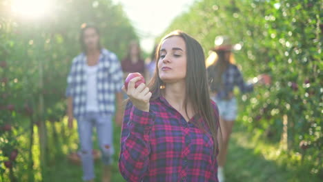 young woman eating an apple in an orchard with friends