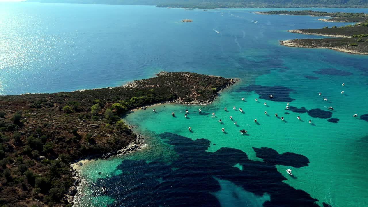 Aerial drone view of the Blue Lagoon in Halkidiki, Greece turquoise crystal waters, anchored boats, and rocky coastline surrounded by lush Mediterranean vegetation