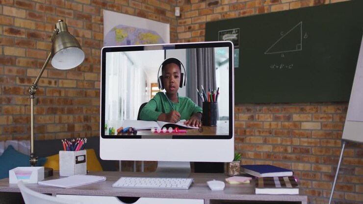 Ragazzo afroamericano che segue una lezione scolastica online sullo schermo del computer sulla scrivania