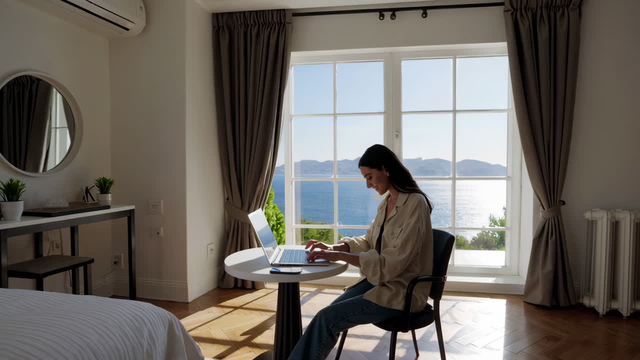 Woman working on a laptop in a hotel room with a beautiful ocean view