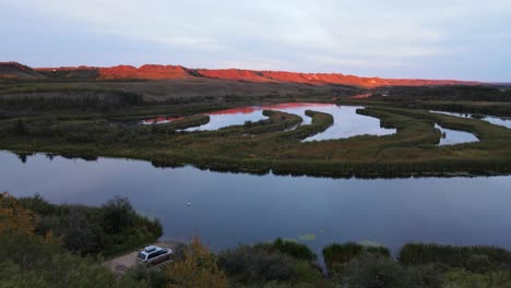 last orange sunlight illuminating the peaks of a mountain range in southern alberta with beautiful reflections on the calm river in front