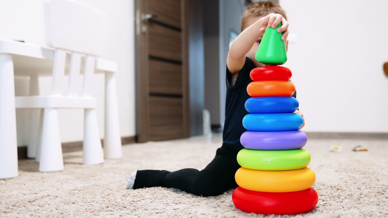Baby boy puts the top detail of top pyramid on the toy. Kid disassembles the attached part and puts on the floor.