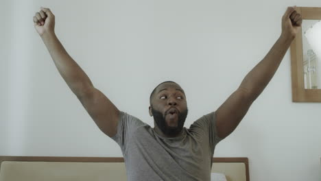 Young-guy-outstretched-arms-in-bed-in-morning.-Black-man-dancing-in-bed.