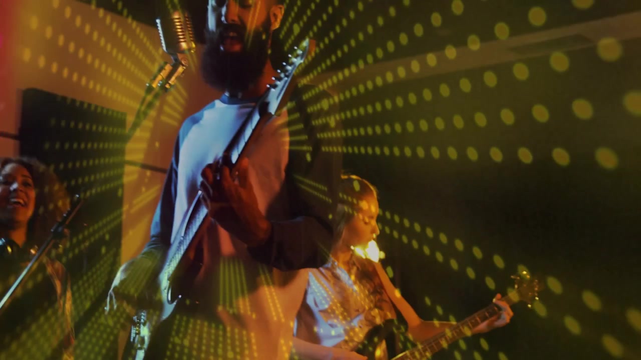 Cantante frontman con maglietta raglan che suona la chitarra sul palco con un microfono vintage e una proiezione verde.