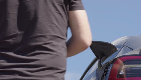 closeup - the owner unplugs his electric car and gets in ready to drive, sunny