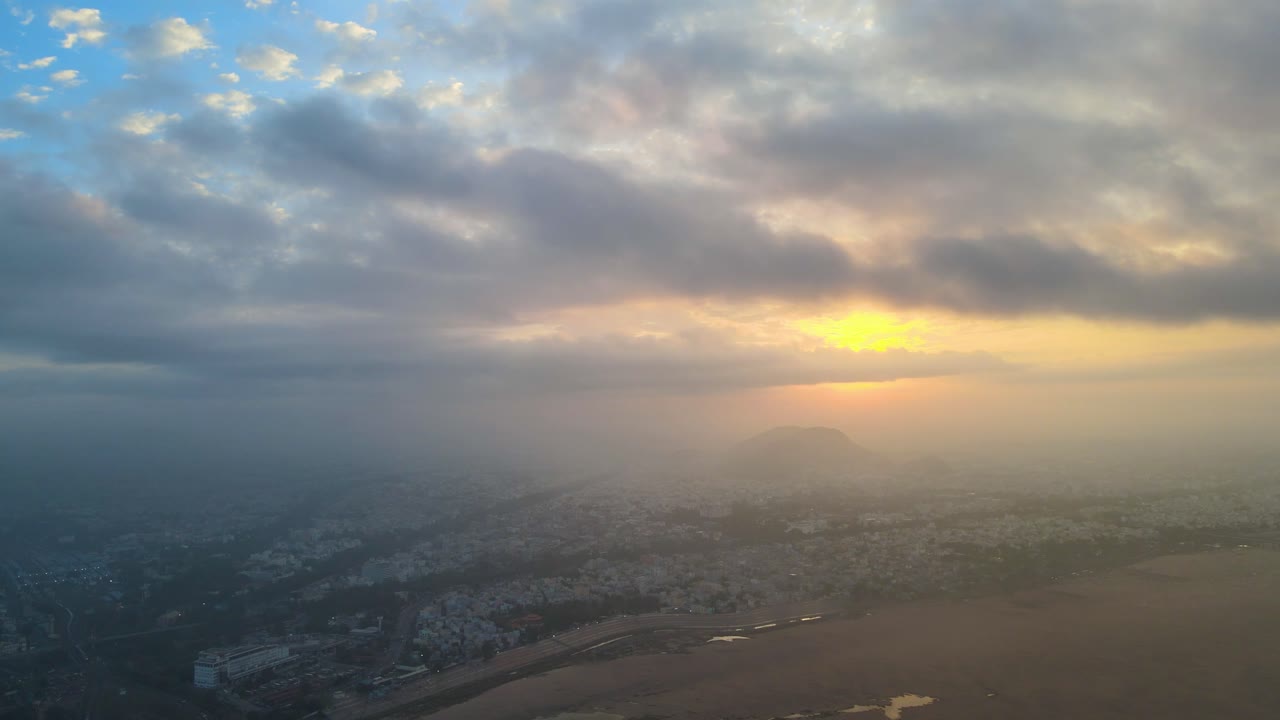 Aerial drone shot highlighting Vijayawada’s vibrant cityscape during sunrise, with floating clouds adding a dreamy effect.