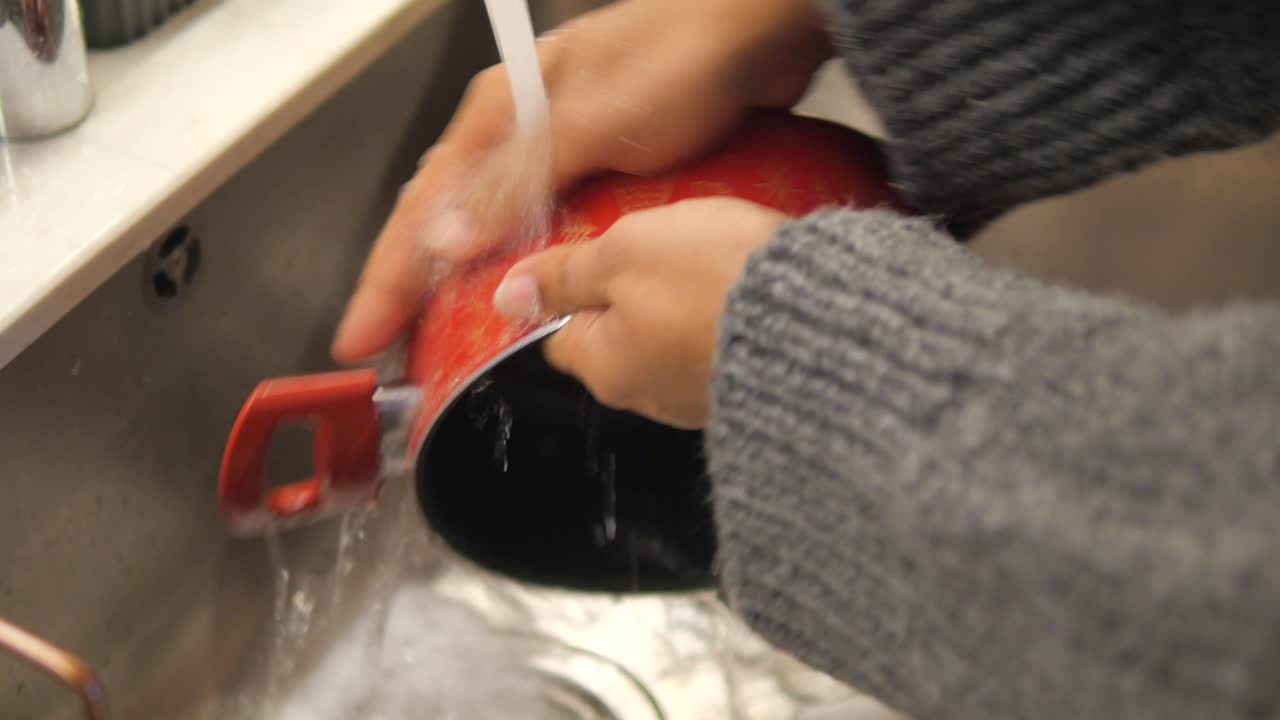 mujer lavando una olla roja en el fregadero de la cocina