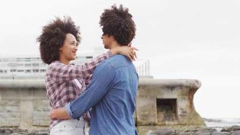 pareja afroamericana abrazándose en las rocas cerca del mar