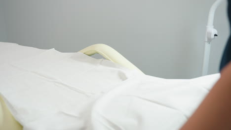 skin care expert in navy uniform sprays antiseptic onto cotton pad and carefully wipes down pale massage chair in pristine white treatment room, ensuring hygienic surface and welcoming environment