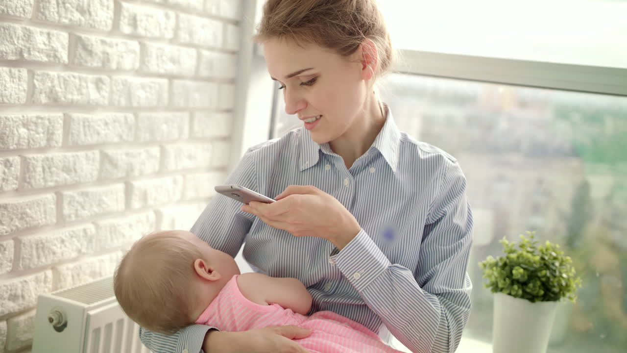 hermosa mujer en camisa tomando una foto móvil de la niña. mamá tomando una foto del bebé