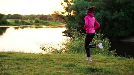 a girl in a pink jacket and black pants runs near the river in headphones preparing for the marathon