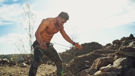 healthy bodybuilder doing workout with stones. strained muscular athlete throwing big stones on the rocky background. slow motion.