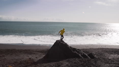 young male traveler throwing a stone into the ocean on black sand beach in iceland