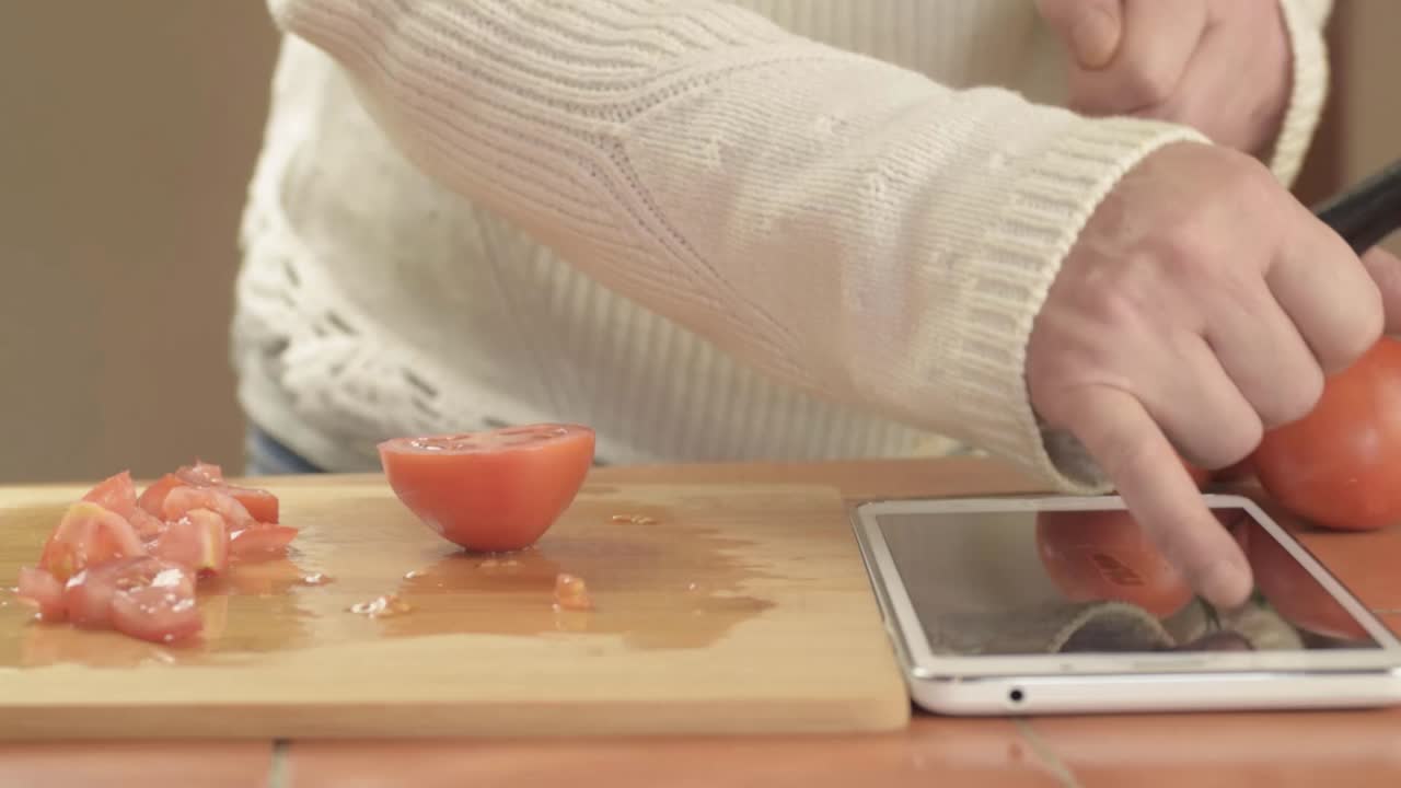 Hands preparing fresh vine tomatoes in kitchen with recipe on tablet medium shot