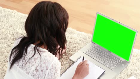 mujer sonriente acostada en el suelo haciendo la tarea usando una computadora portátil