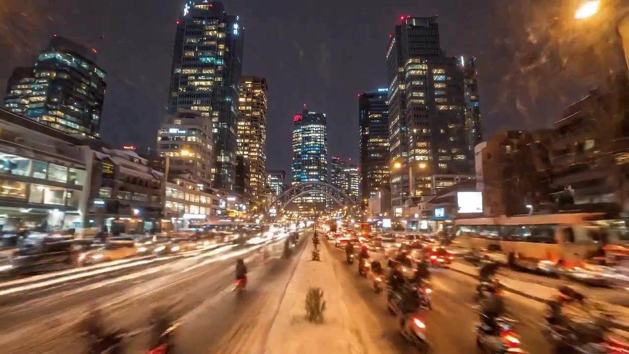 Un vivace paesaggio urbano illuminato dal crepuscolo, che mostra grattacieli circondati da strade innevate, traffico intenso e un'atmosfera invernale dinamica al tramonto.
